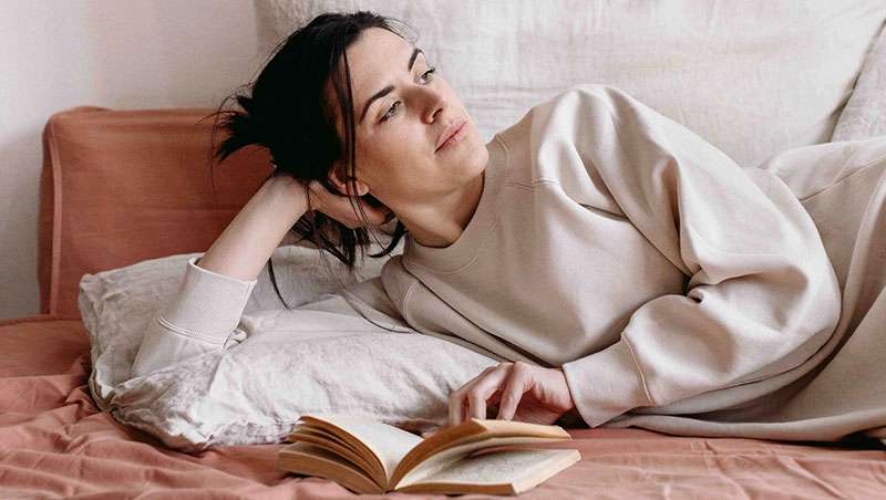chica morena tumbada pijama leyendo libro